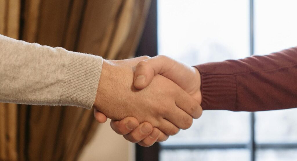 A close-up of two adults shaking hands indoors beside a window.